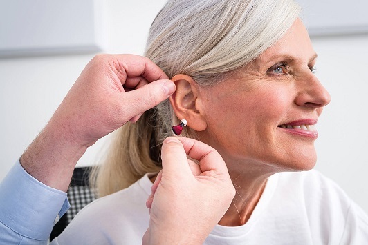 Seniorin bekommt ein modernes Hörgerät ins Ohr eingesetzt, Hörhilfe für Schwerhörigkeit.